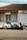 Two motor scooters are parked in front of a storefront with a tiled roof. The building has a closed sliding shutter on one side and a glass door with curtains on the other, above which is a sign that reads 'SHERLY Shop'. The pavement is patterned, and there are power lines visible overhead.