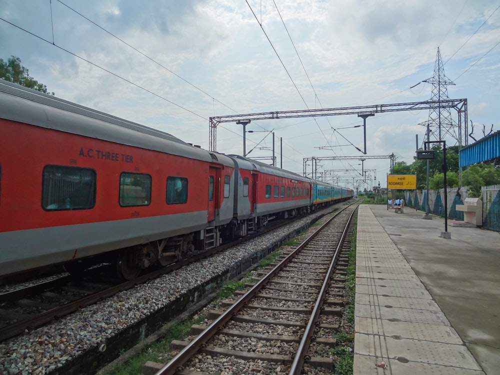 a red train traveling down train tracks next to a loading platform