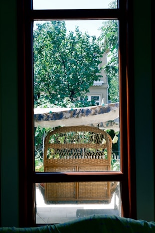 Close-up of a handwoven wicker patio chair with plush cushions surrounded by lush greenery.