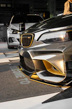 A close-up of a shiny black car with a fresh gold-accented paint job inside a modern auto body shop.