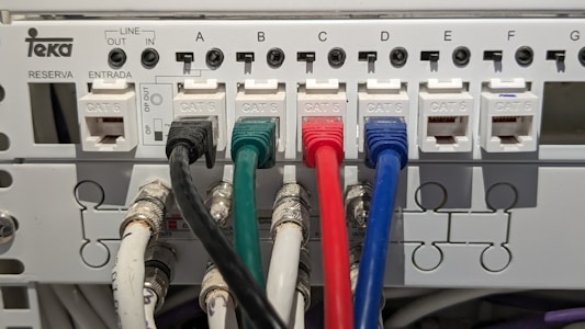 An electrical panel with multiple Category 6 (CAT 6) ethernet cables plugged into ports labeled from A to G. The cables are of different colors, including black, green, red, and blue, organized neatly into corresponding outlets. The panel includes labels for 'LINE OUT' and 'LINE IN' and the brand name 'Teka' is visible.
