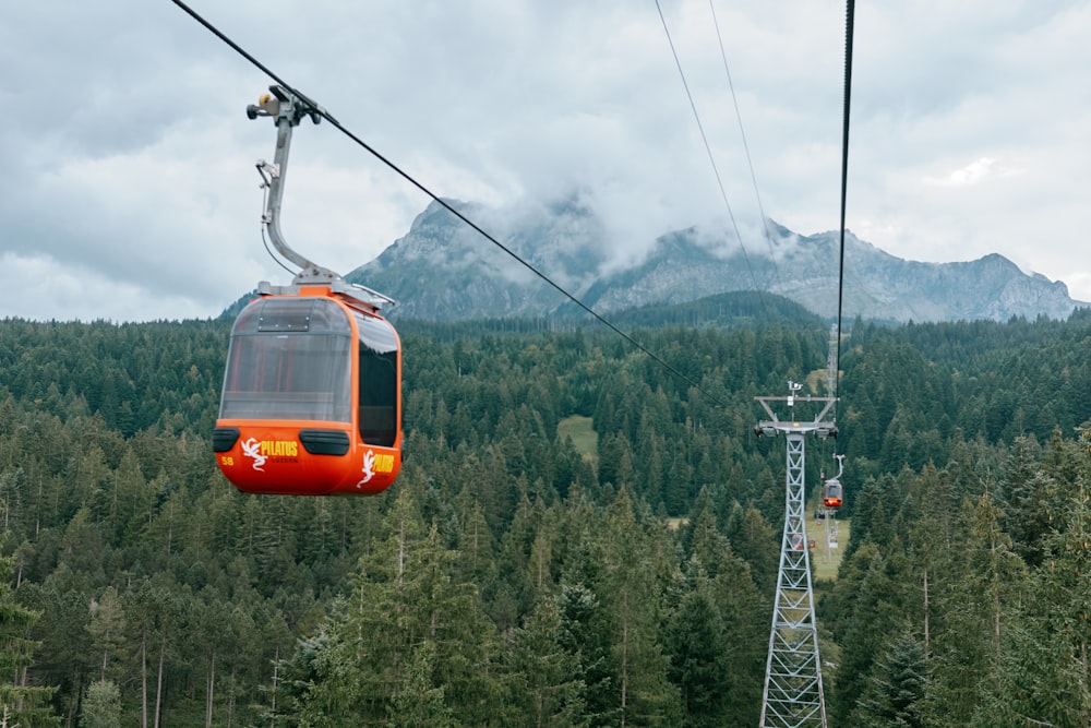 a cable car going over a forest with a mountain in the background