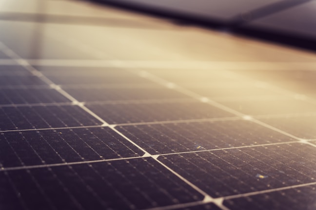 A close-up of solar panels featuring a grid of dark photovoltaic cells arranged in a linear pattern. The soft lighting creates a gradient effect across the surface, enhancing the reflective quality of the panels.