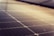 A close-up of solar panels featuring a grid of dark photovoltaic cells arranged in a linear pattern. The soft lighting creates a gradient effect across the surface, enhancing the reflective quality of the panels.