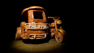 A miniature tricycle model with the word 'Philippines' displayed prominently on the front. The model is crafted to resemble a real motorized tricycle, a common mode of transportation in the Philippines, and is illuminated against a dark background, highlighting its details.