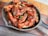 A cast iron skillet filled with crispy chicken wings drizzled with a rich, glossy barbecue sauce and garnished with finely chopped green onions. The skillet is placed on a wooden surface.