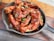 A cast iron skillet filled with crispy chicken wings drizzled with a rich, glossy barbecue sauce and garnished with finely chopped green onions. The skillet is placed on a wooden surface.