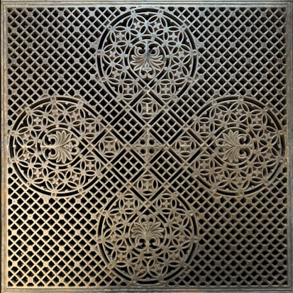 A decorative, intricate metal grate featuring symmetrical floral patterns and geometric shapes. The design consists of circular motifs with ornate floral embellishments and a lattice background, giving it a classic and artistic appearance.