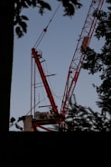 Red and black spider crane lifting materials on a construction site at sunset.