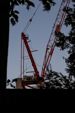 Red and black spider crane lifting materials on a construction site at sunset.