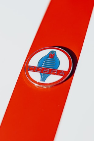 A close-up view of an emblem featuring a stylized blue cobra on a white circle with a red background. The word 'COBRA' is written below the snake in bold, red letters. The emblem is set against a bright orange stripe that contrasts with the white base color.