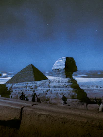 An atmospheric night view of the pyramids illuminated by moonlight against a starry sky.