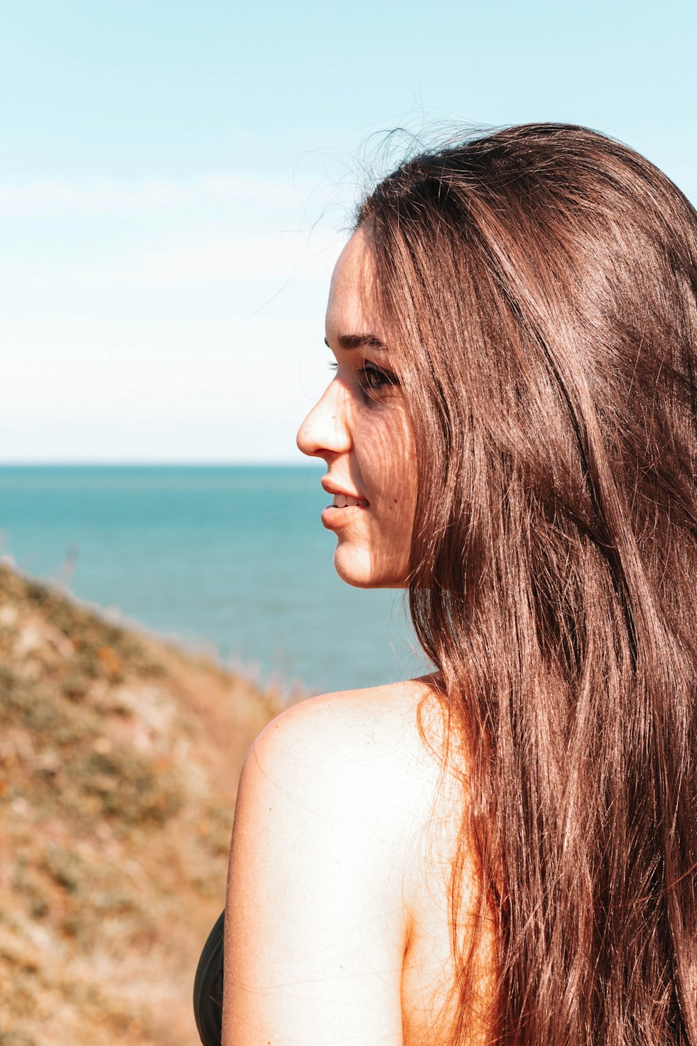 a woman with long brown hair standing next to the ocean