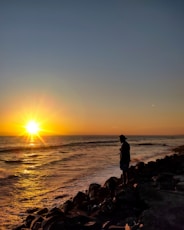 a person standing on a rocky beach at sunset