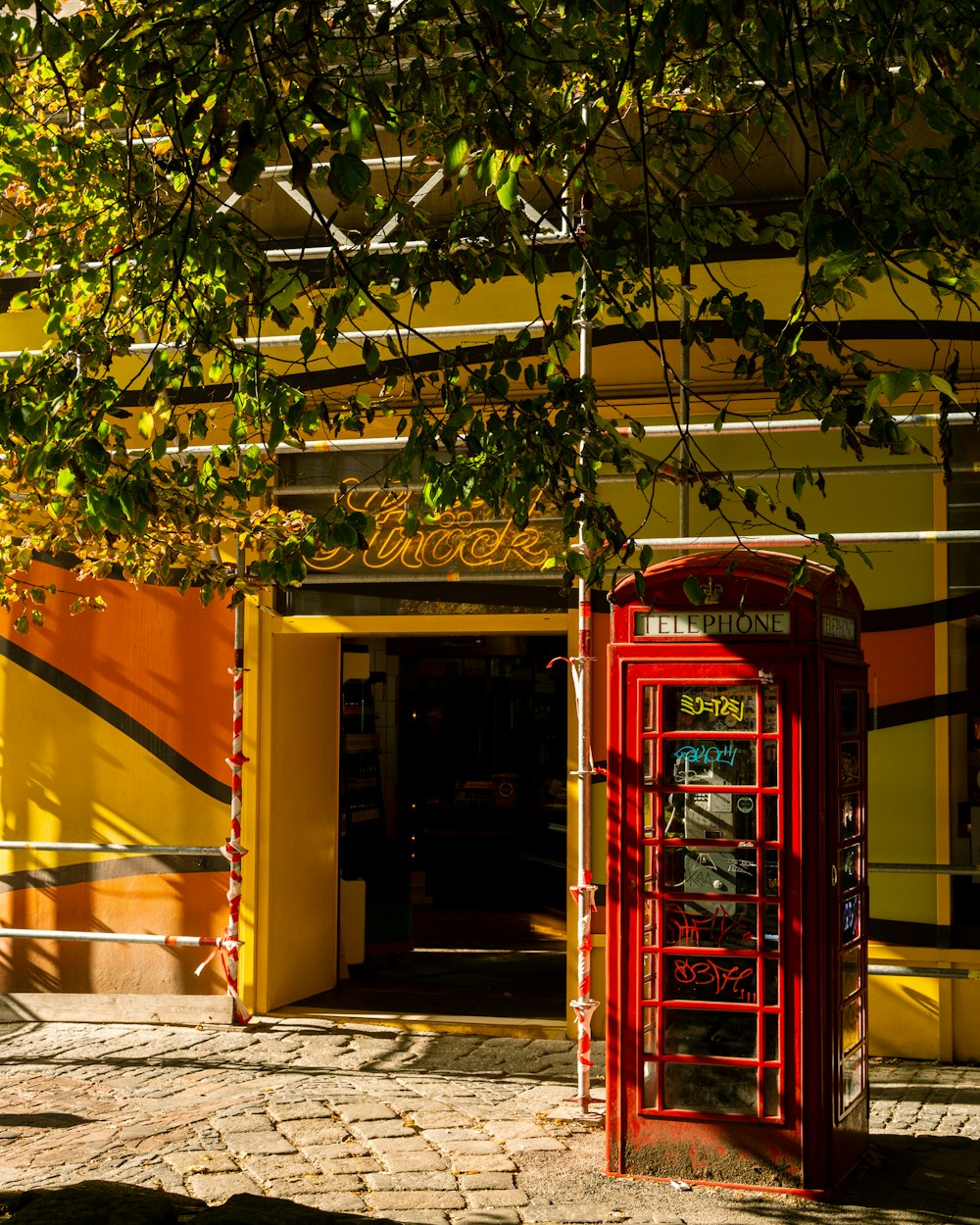 a red phone booth in front of a yellow building