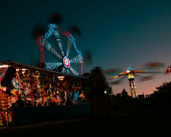 A ferris wheel and carnival rides lit up at night at an outdoor fair