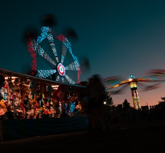 a carnival with a ferris wheel lit up at night