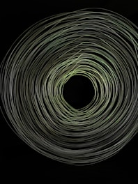 A swirling vortex of light trails against a dark background, forming concentric circular patterns that create an impression of depth and motion.