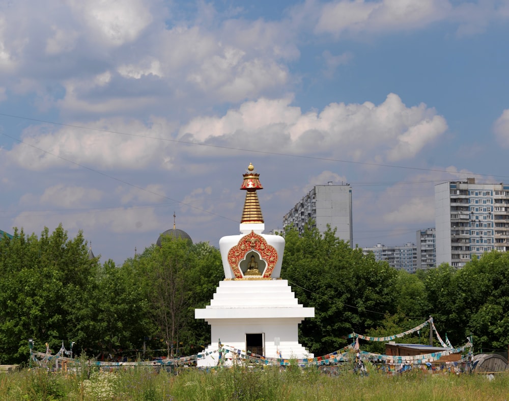a white and gold statue in a field with buildings in the background