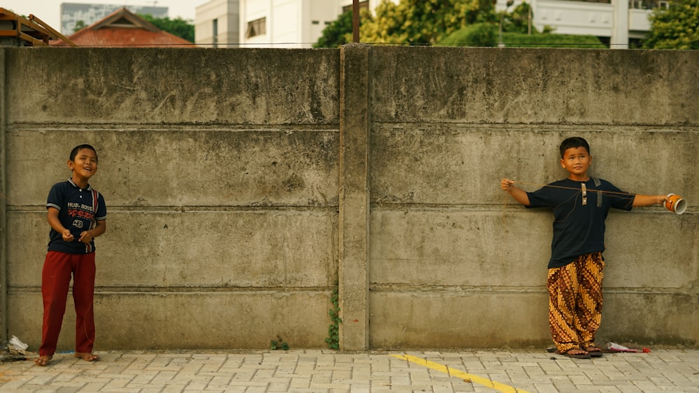 a couple of kids standing next to a cement wall