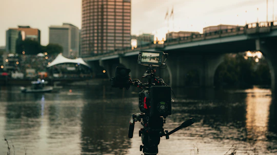 A filmmaker adjusting a camera on location capturing a vibrant cityscape at sunset.