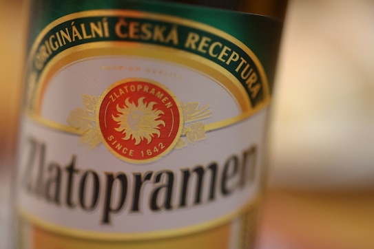 A close-up of a beer bottle label with the word Zlatopramen prominently displayed in large, bold font. The label is detailed with a green, gold, and red color scheme. The text 'Originaln&iacute; Česk&aacute; Receptura' is written at the top, and a red emblem with a sun logo and 'Since 1642' is in the center.