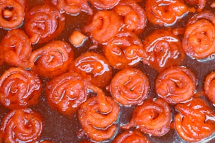 Close-up of vibrant rasgullas soaked in syrup with saffron strands and pistachio garnish.