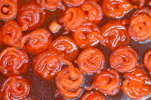 Close-up of vibrant rasgullas soaked in syrup with saffron strands and pistachio garnish.