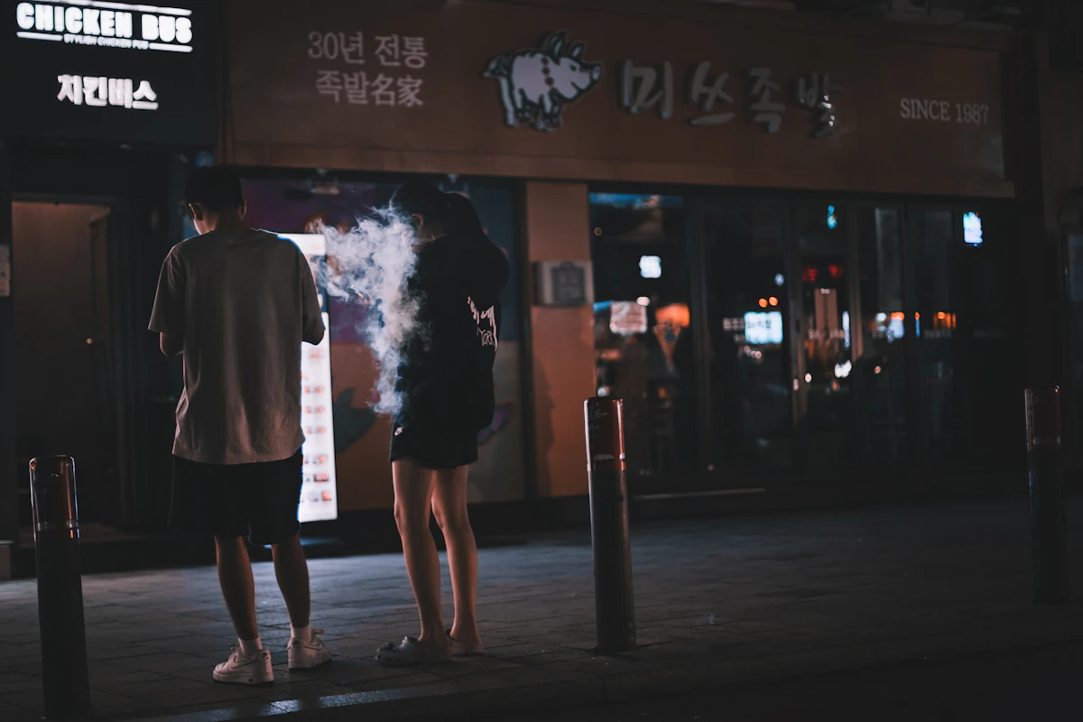 Two people seen from behind outside a lit restaurant at night near Hongik University Station
