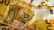 A golden Bitcoin physical coin is placed on top of several Euro banknotes. The banknotes display architectural imagery and a mix of colors including yellow, brown, and red, with the Bitcoin logo prominently visible on the coin.