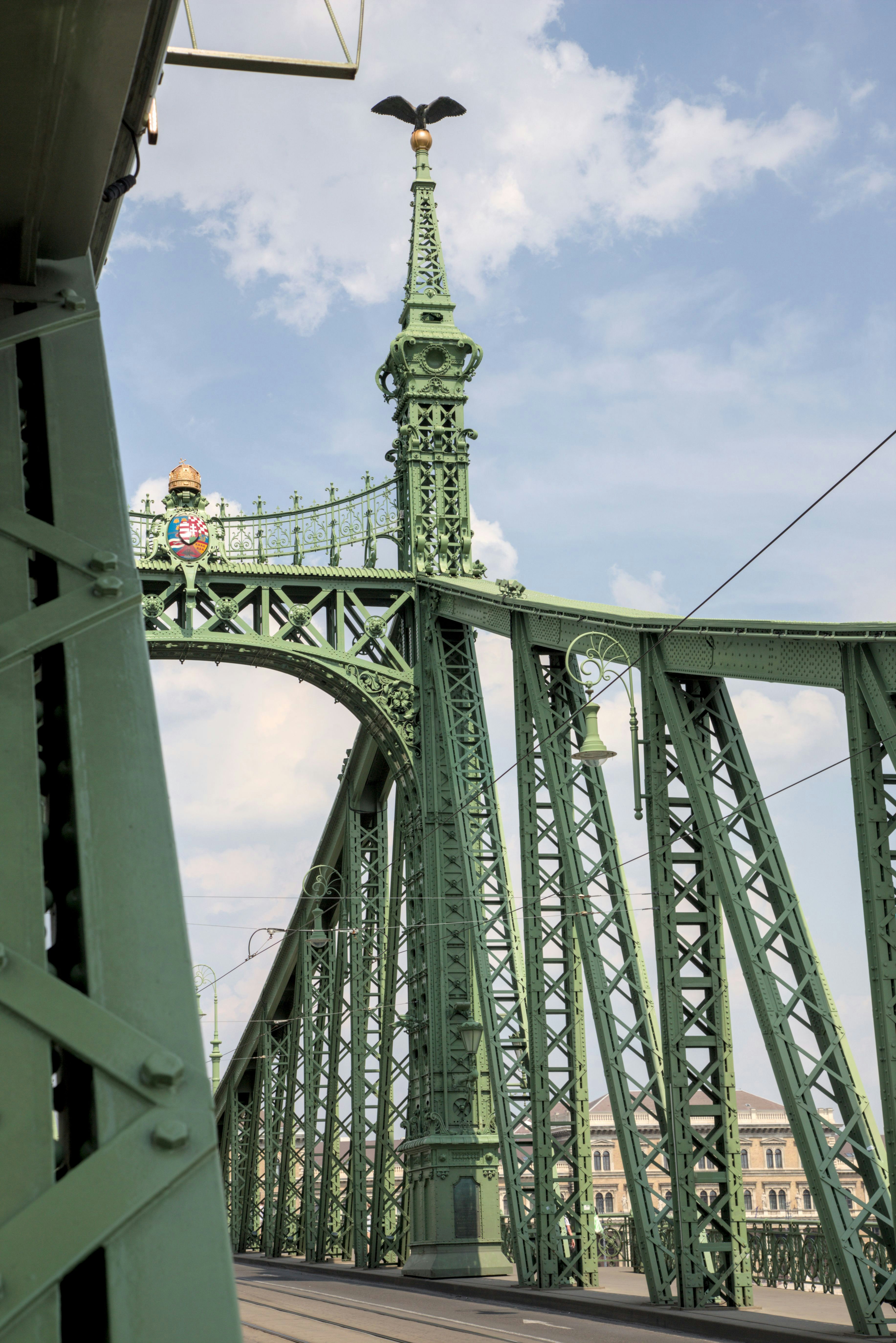 A green bridge with a clock tower in the background photo – Free Bridge ...