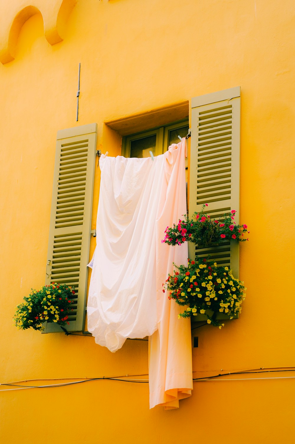 a yellow building with green shutters and flowers