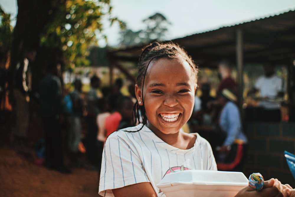 a young girl smiles as she holds a bowl of food