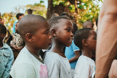 Children attending an outdoor class under a large tree, engaged and curious.