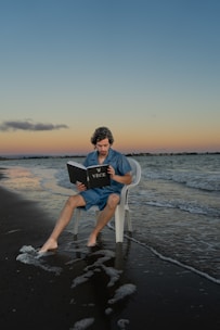 a man sitting in a chair on the beach reading a book
