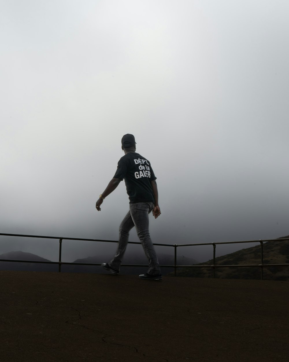 a man walking across a dirt field next to a fence