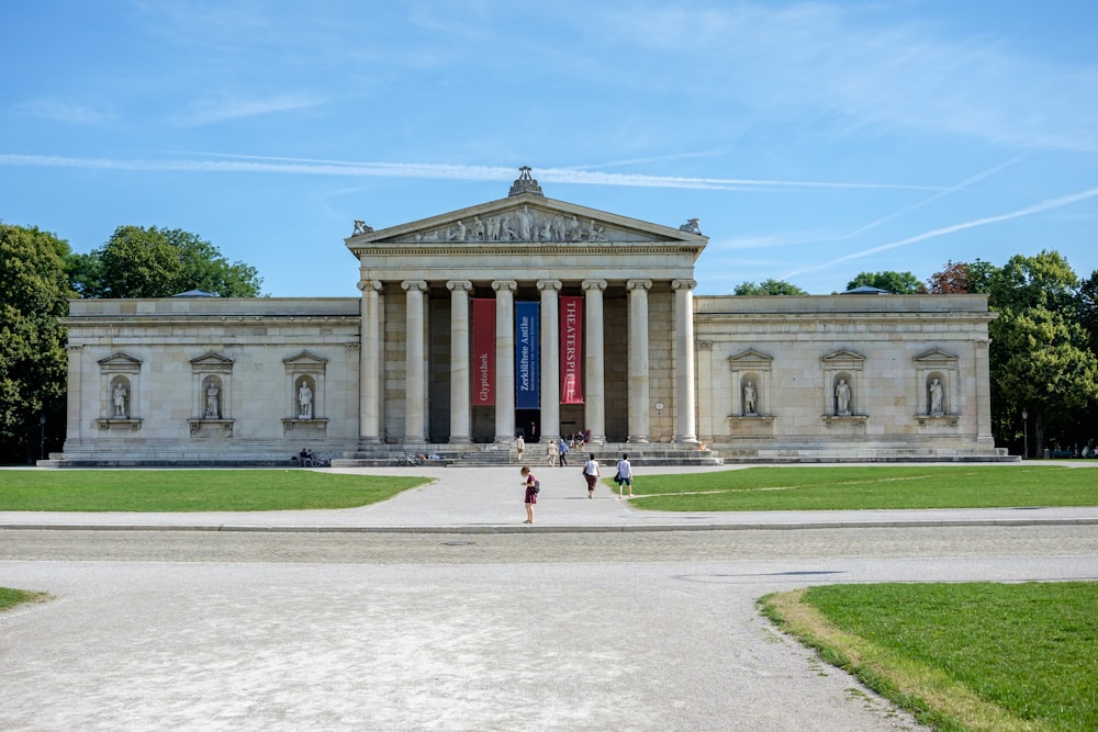 a large building with two columns and two people walking in front of it