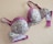 A floral-patterned bra with pink lace detailing and purple straps, laid flat on a beige surface. The cups and band feature a light green fabric adorned with small pink and white flowers.