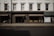 The image captures a storefront with large windows displaying various decorative items like vases and small furniture pieces. The facade has a classic architectural design with white upper walls and large, vertical windows situated above the black-framed shop displays. The street in front of the store is empty, and a billboard on the side advertises 'London Design Week'.