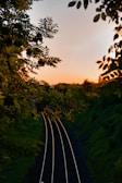 A vibrant sunset over a rural Thai railway track winding through lush green fields.