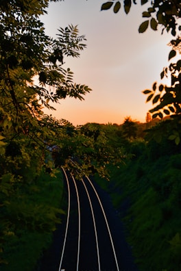 A vibrant sunset over a rural Thai railway track winding through lush green fields.