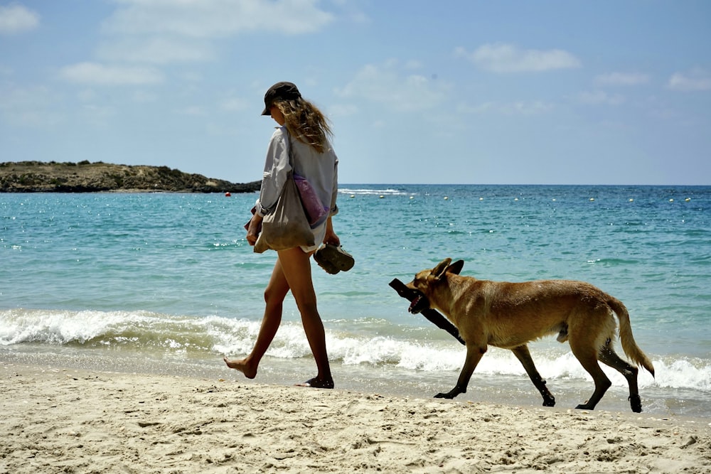 a woman walking on a beach next to a dog