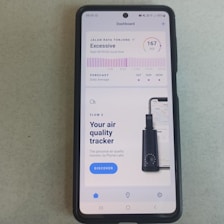 A smartphone displays an application about air quality. The screen reads an 'Excessive' air quality level with an AQI of 167. There is a chart showing a forecast for daily average air quality levels. Below, there's an advertisement for an air quality tracker device by Plume Labs with a 'Discover' button.