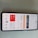 A smartphone displaying an air quality monitoring app interface in Indonesian, featuring an AQI reading of 159, which is labeled as unhealthy. The screen is divided into sections with different readings and options, and the phone is placed on a light grey surface.