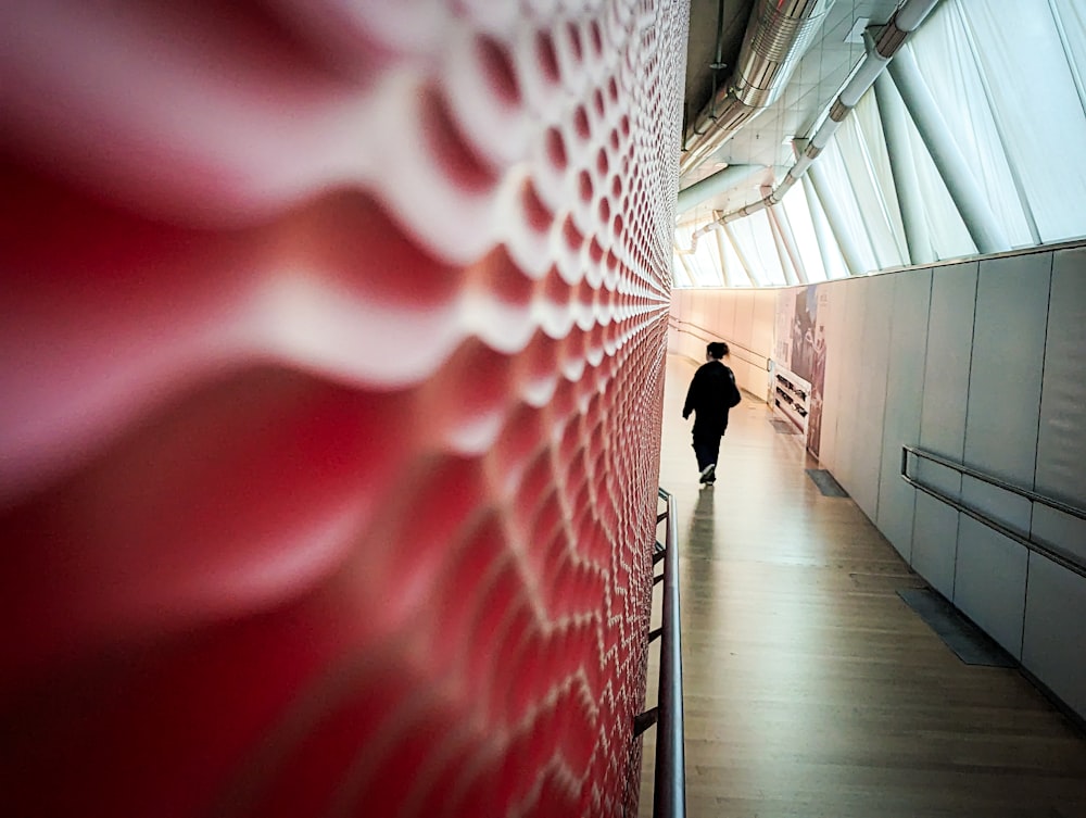 a man walking down a hallway next to a red wall