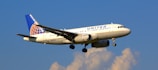 A commercial airplane with the United Airlines logo is flying against a backdrop of a clear blue sky with some clouds. The aircraft is white with blue and gold accents, and its wings are spread wide.