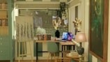 a room with a desk, chair, bookshelf and a laptop