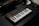 A small MIDI keyboard controller rests on a dark surface, featuring black and white keys along with various knobs and pads. The branding 'Akai MPK mini' is visible on the device. The lighting is low, giving it a professional studio ambiance.