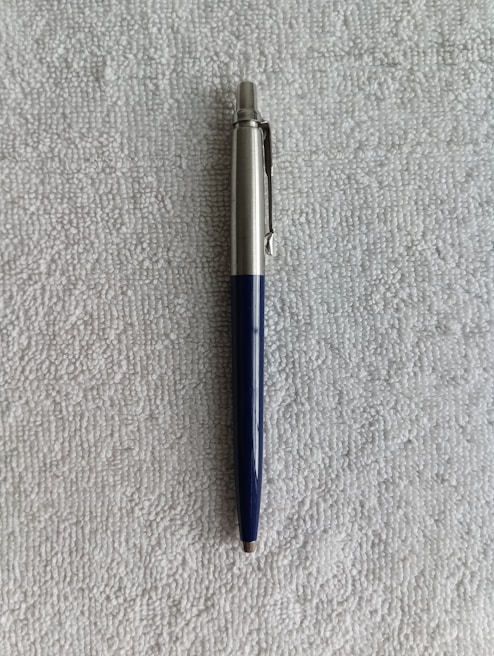 A ballpoint pen with a silver upper body and a dark blue lower body is resting on a textured gray surface.