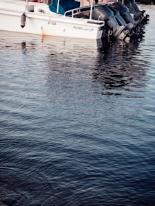 A motorboat docked on calm water, with several outboard engines. The upper part of the boat has a canopy and safety railing, while the hull displays the name 'Alhaj marine' and identification number JF-324.